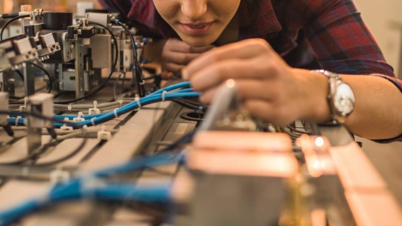Smiling engineer student examining part of production line in a laboratory.